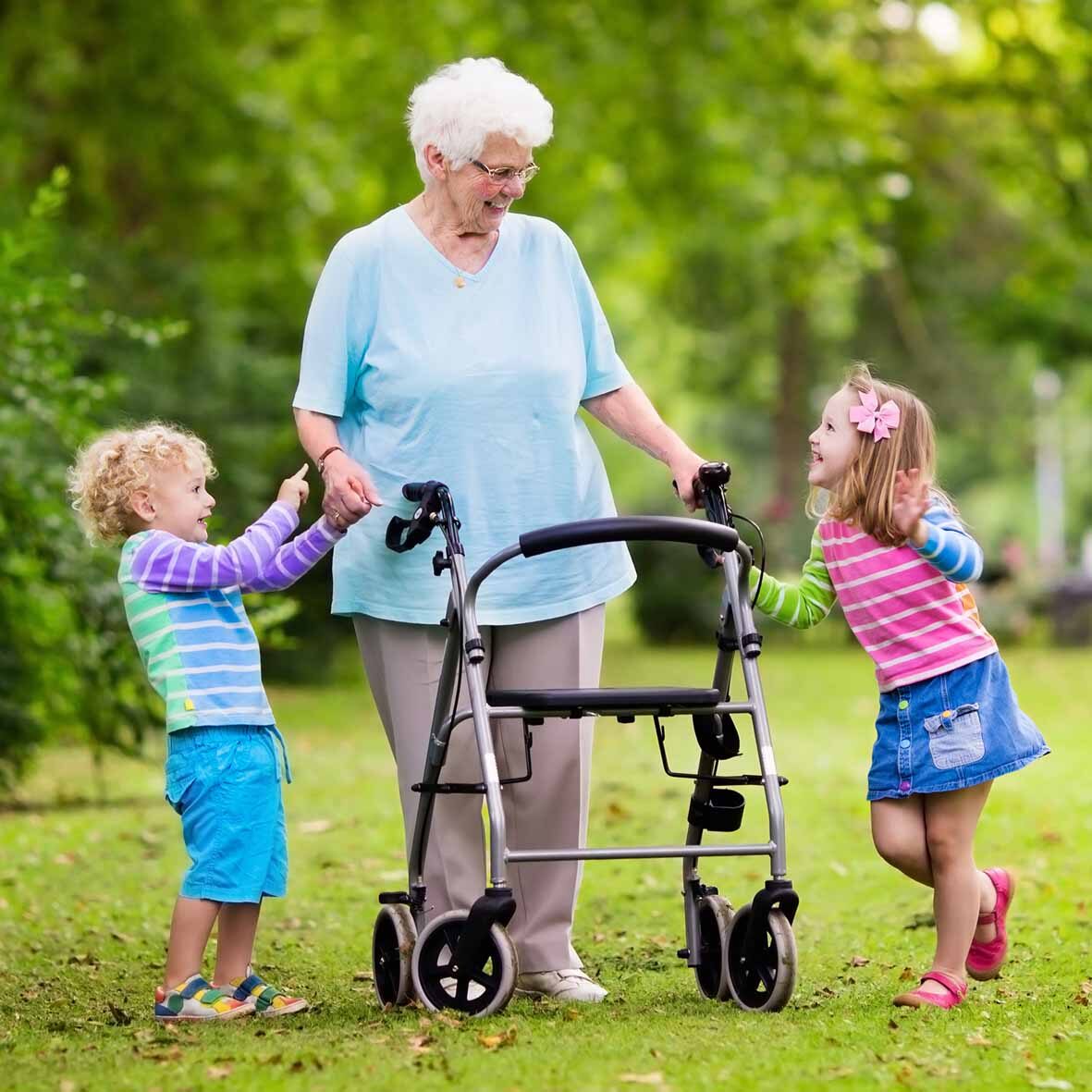 An elderly woman using a walking aid smiling with two children