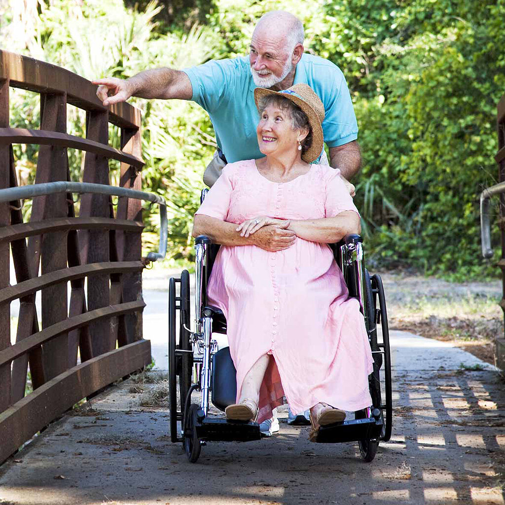 A man pushing a woman in a wheelchair across a wooden bridge